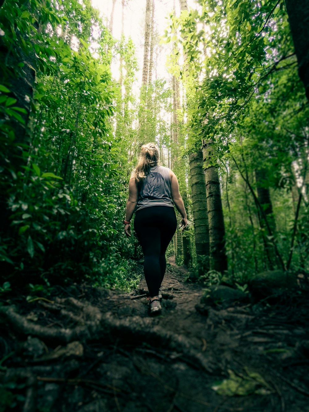 woman in black tank top and black leggings standing in the middle of forest during daytime