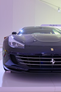 A sleek, black luxury sports car is displayed. The car features a prominent emblem on the front, smooth aerodynamic lines, and a shiny exterior. It is positioned indoors under bright lighting, highlighting its glossy finish and modern design.