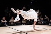 man in white dress shirt and white pants jumping on brown wooden floor