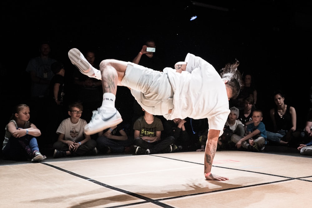 man in white dress shirt and white pants jumping on brown wooden floor