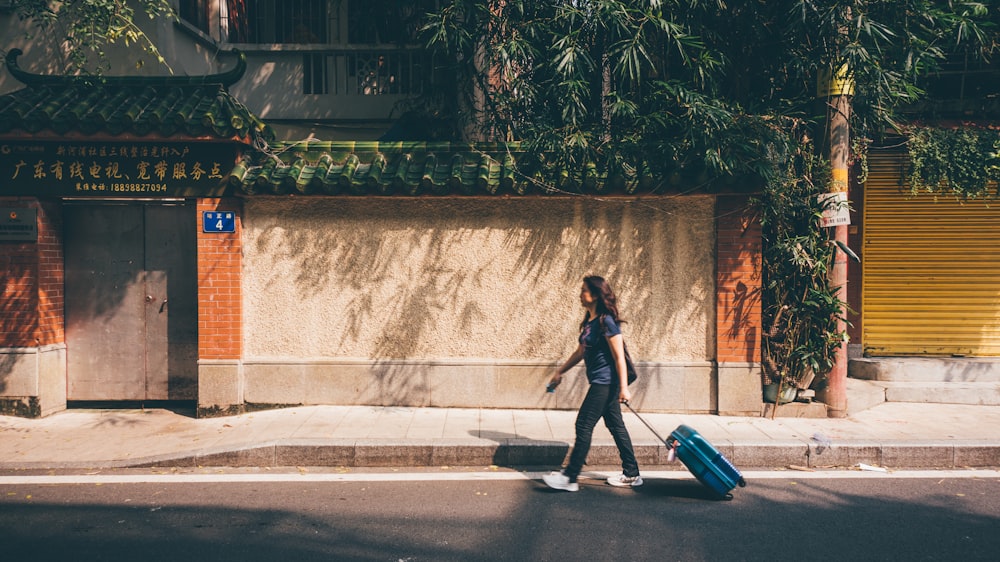 woman in black long sleeve shirt and black pants standing beside blue luggage bag during daytime