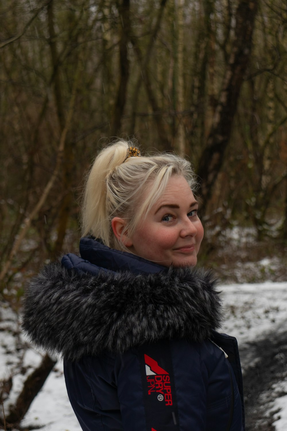 woman in black fur coat standing near trees during daytime