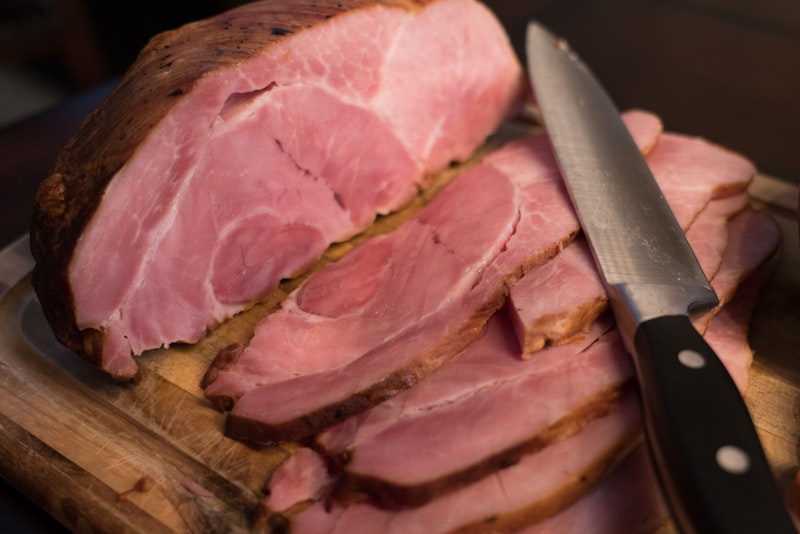 Sliced cured ham on a wooden board with a carving knife