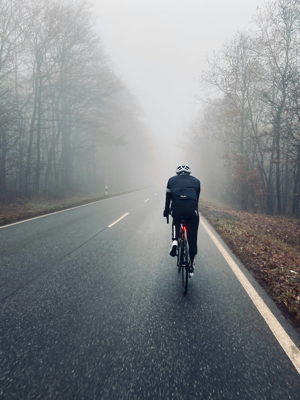 homem na jaqueta preta que monta a bicicleta na estrada durante o tempo nebuloso