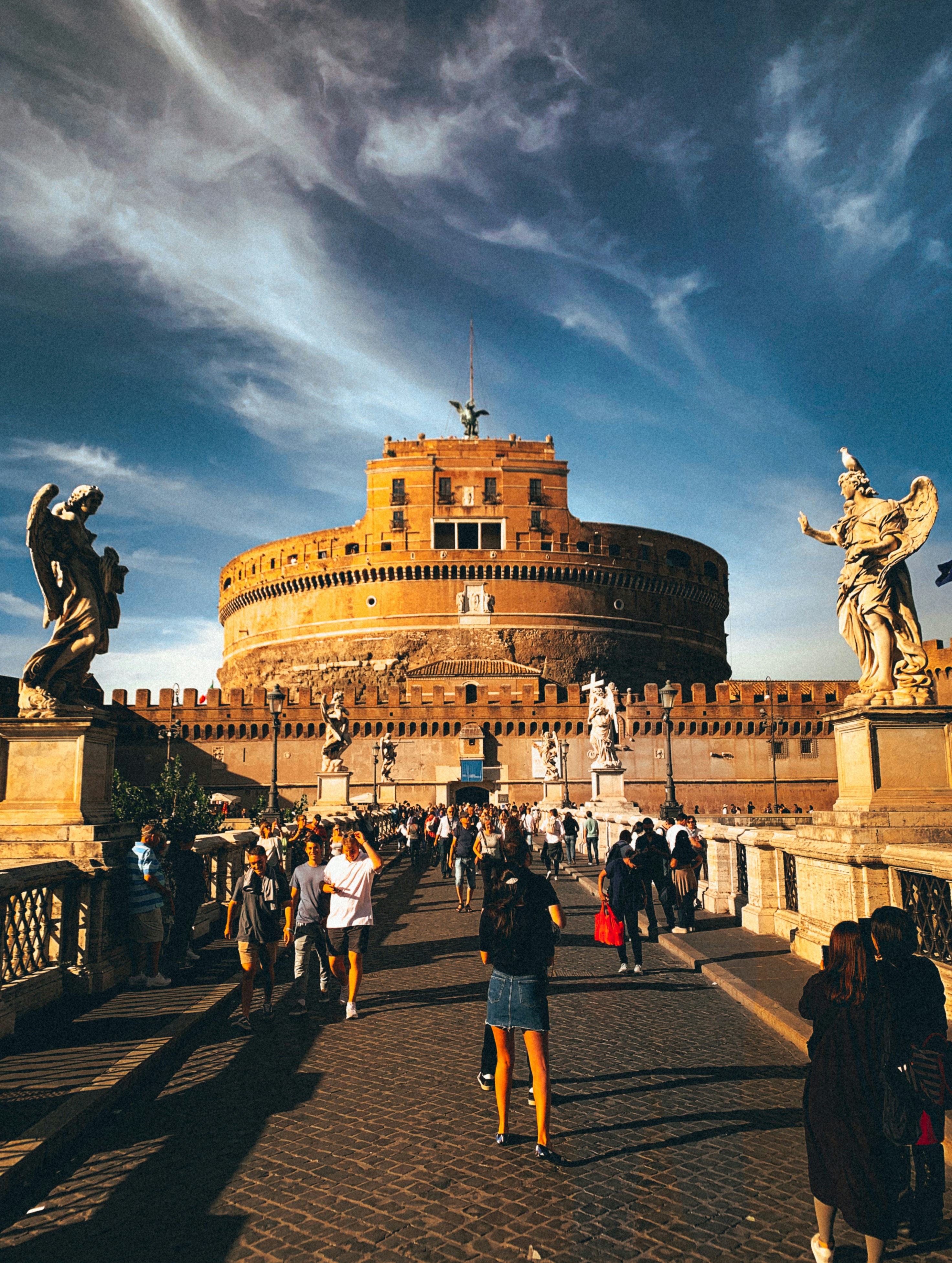 people walking on street near brown concrete building under white clouds and blue sky during daytime