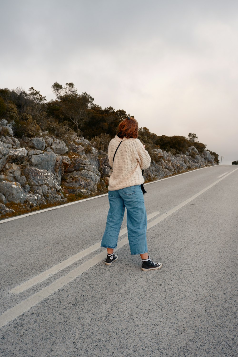 woman in brown jacket standing on gray asphalt road during daytime