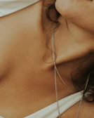 Close-up of a woman's collarbone adorned with a subtle pearl pendant, set against a creamy champagne backdrop.