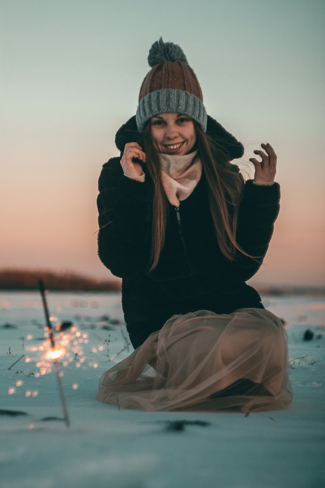 woman in black jacket and brown hijab sitting on snow covered ground during sunset