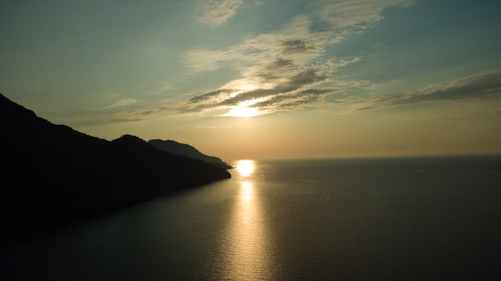 silhouette of mountain beside body of water during sunset