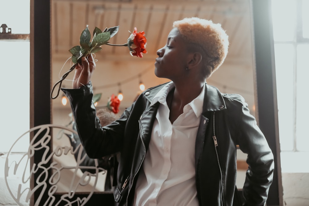 man in black suit jacket holding red rose