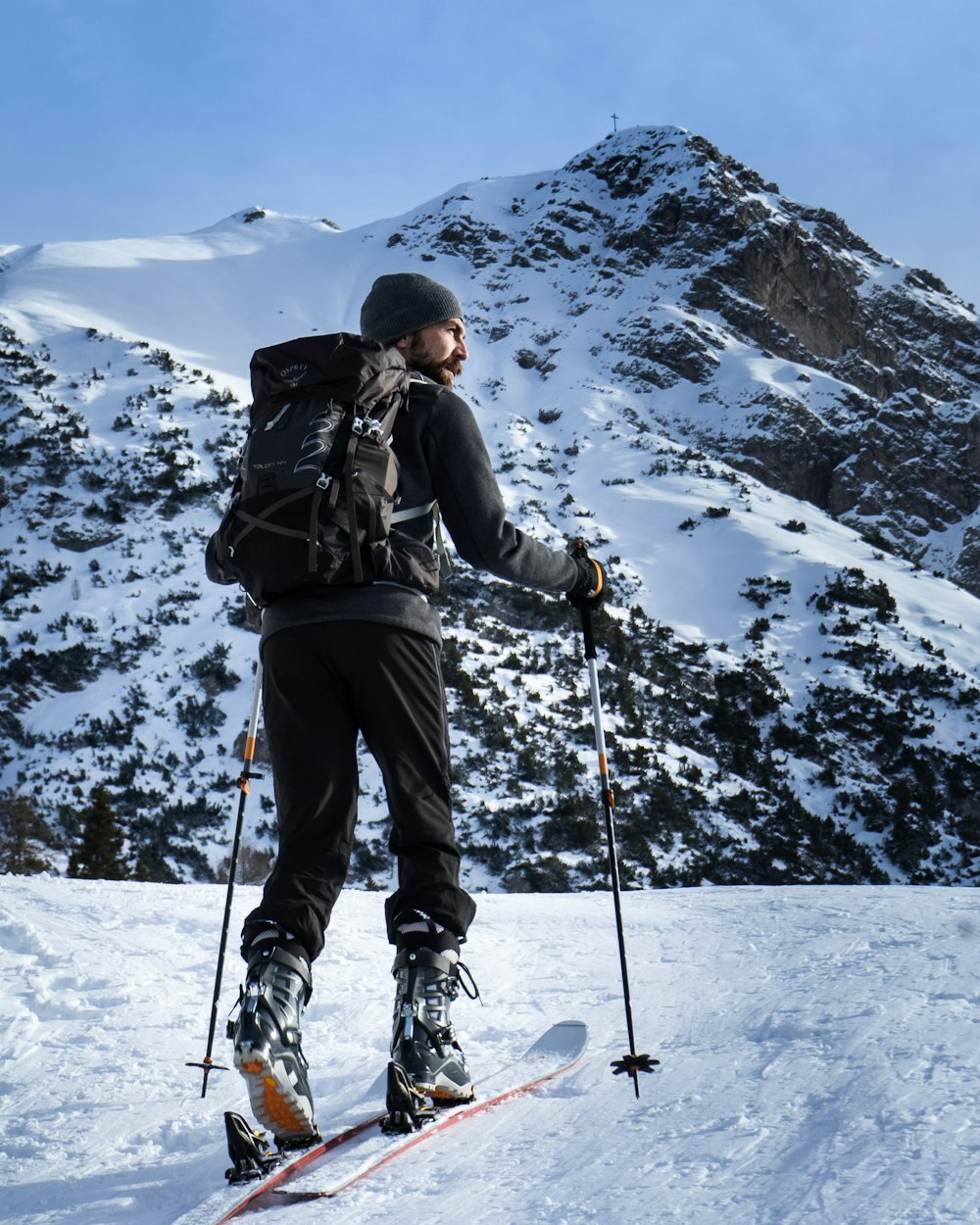 Mann in schwarzer Jacke und blauer Hose, der tagsüber auf einem schneebedeckten Berg steht