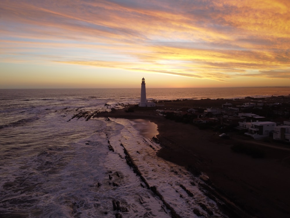 faro bianco su sabbia grigia durante il tramonto