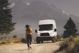 man in brown shirt and black pants standing beside white van during daytime