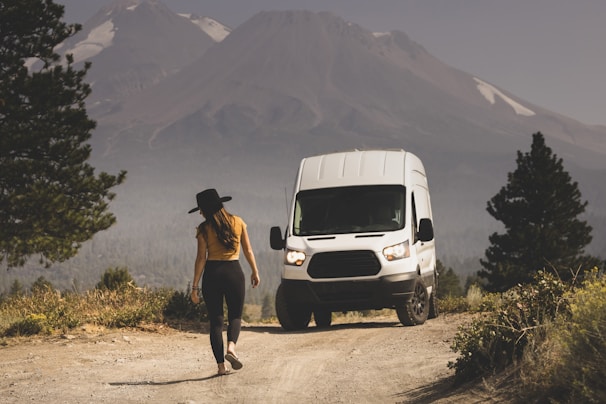 man in brown shirt and black pants standing beside white van during daytime