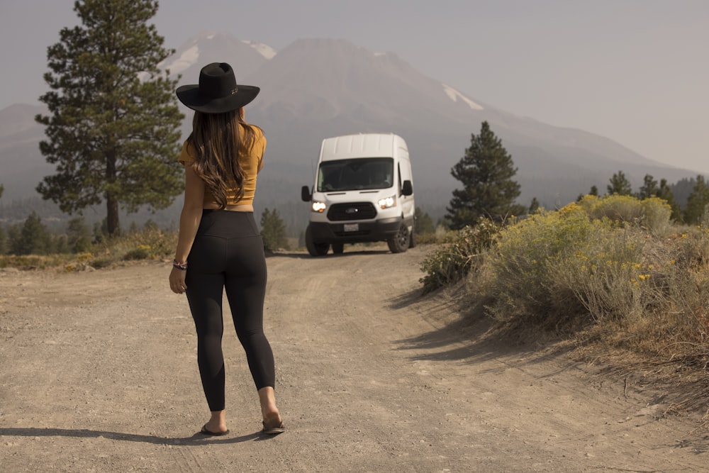 갈색 긴팔 셔츠와 검은 바지를 입은 여자가 낮 동안 회색 도로에 서 있다