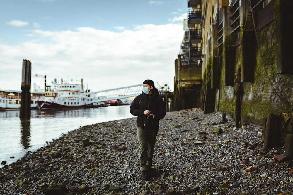 man in black jacket and black pants standing on rocky shore during daytime