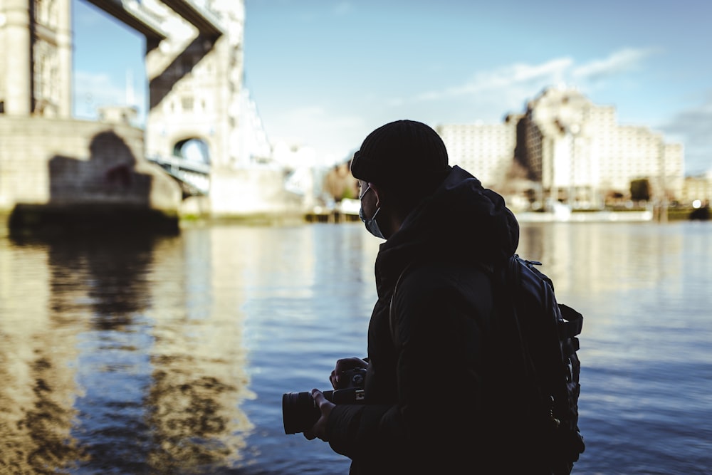 man in black jacket and black sunglasses standing near body of water during daytime