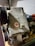 A mechanical component with multiple pulleys is placed on a shelf. The unit appears worn and dusty, suggesting it has been stored or unused for some time. There is a red sticker affixed to its surface, possibly a logo or certification mark.