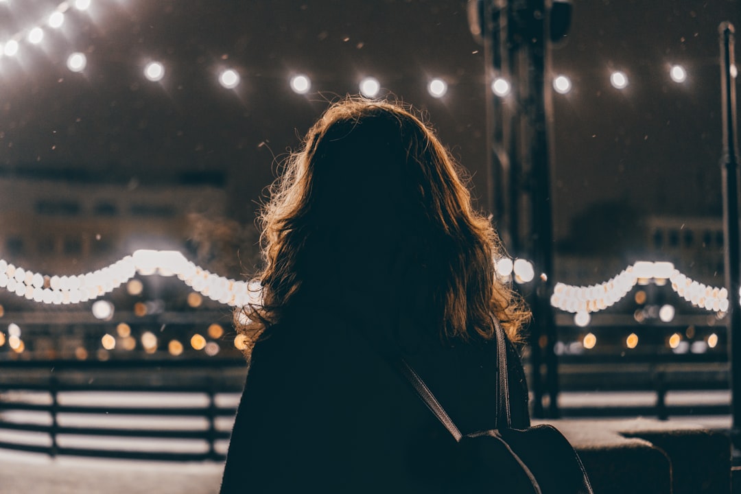 woman in black jacket standing near white string lights during night time
