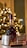 A bottle of Courvoisier V.S.O.P cognac is placed on a table alongside a metal flask, an empty glass, and a cigar. In the background, there are blurred lights resembling a Christmas tree, suggesting a festive atmosphere.