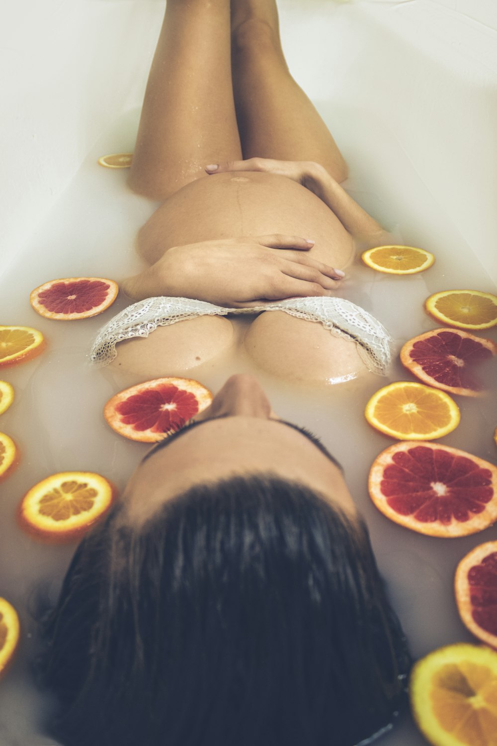 woman in white ceramic bathtub with sliced orange fruits