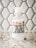 A bottle of hand sanitizer placed on a speckled countertop in front of a hexagonal tile backsplash. The label on the bottle features the text 'El Arroyo' in red and a humorous message about social distancing.