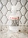 A bottle of hand sanitizer placed on a speckled countertop in front of a hexagonal tile backsplash. The label on the bottle features the text 'El Arroyo' in red and a humorous message about social distancing.
