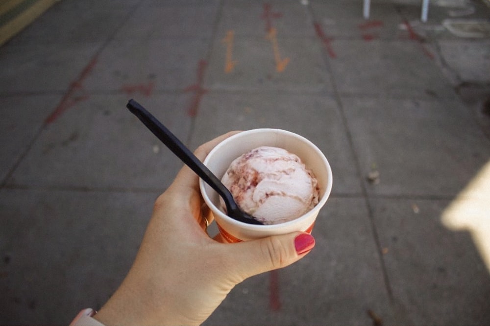 person holding white and red ceramic mug with ice cream