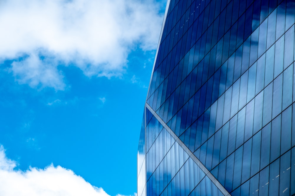 edificio de gran altura con paredes de vidrio azul bajo cielo nublado azul y blanco durante el día