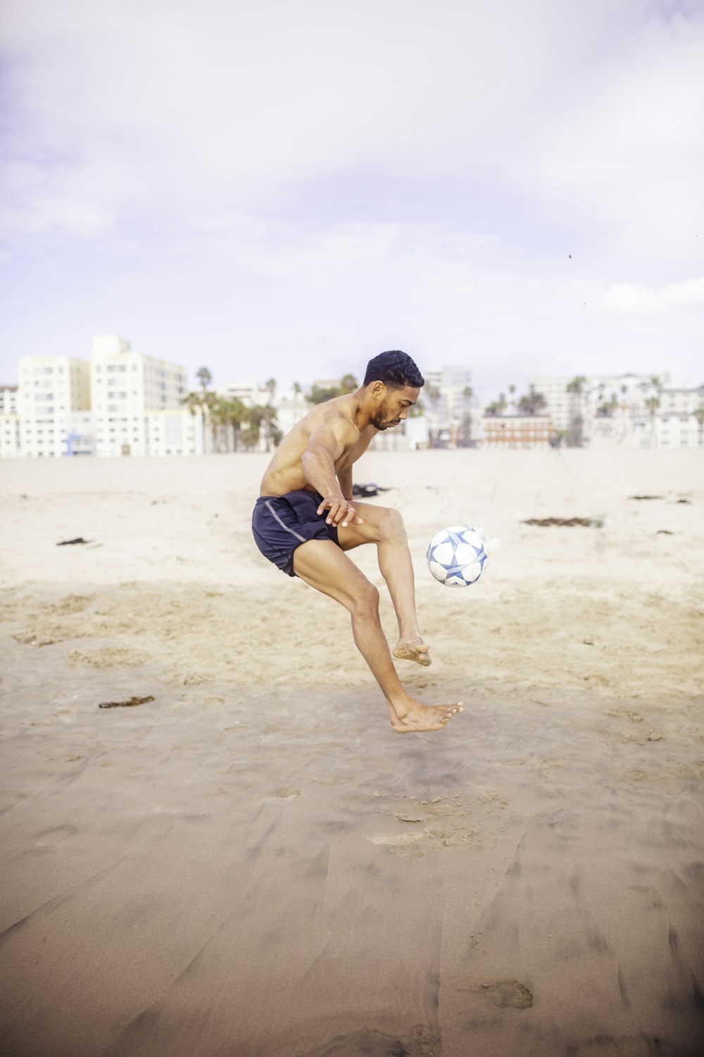 Mann in blauen Shorts spielt tagsüber mit weißem und rotem Fußball am Strand