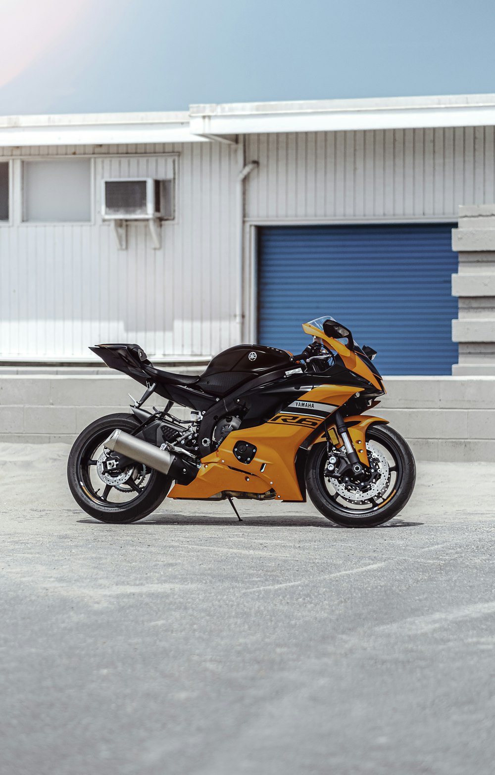 orange and black sports bike parked beside blue and white building