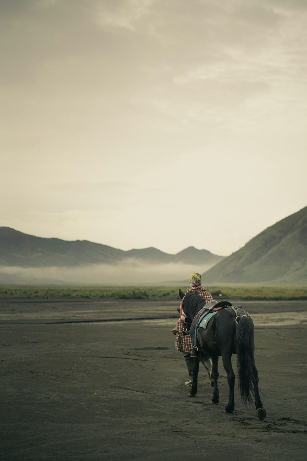 homem que monta a cavalo na areia cinzenta durante o dia