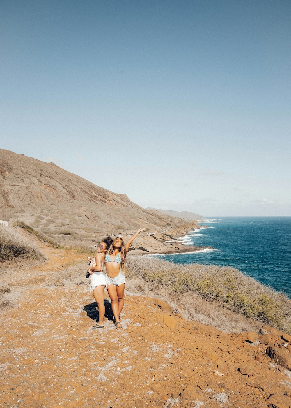 Femme en bikini blanc debout sur un champ brun près de Blue Sea pendant la journée