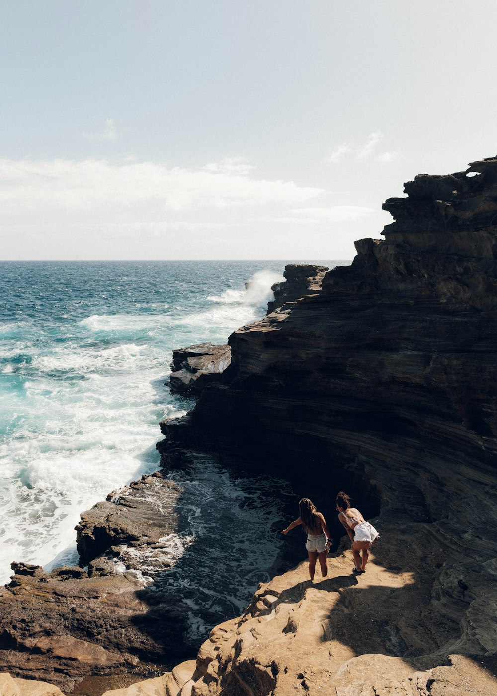 Mujer en bikini blanco sentada en una formación rocosa marrón cerca del mar durante el día