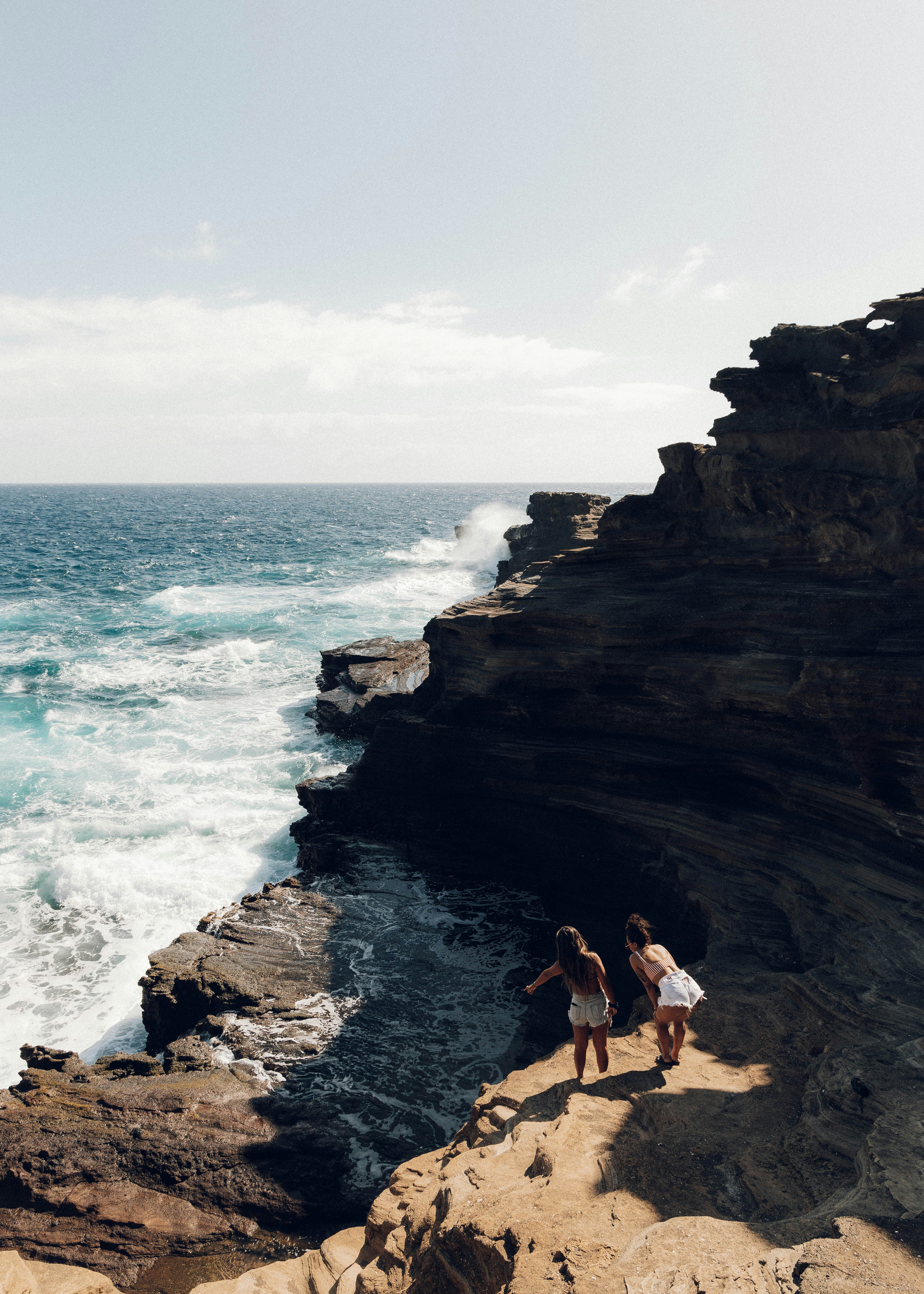 woman in white bikini sitting on brown rock formation near sea during daytime