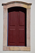 Close-up of a freshly painted wooden door and window frame in deep maroon, highlighting fine brushwork.