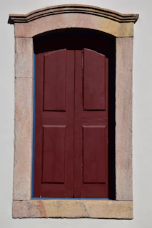 Close-up of a freshly painted wooden door and window frame in deep maroon, highlighting fine brushwork.