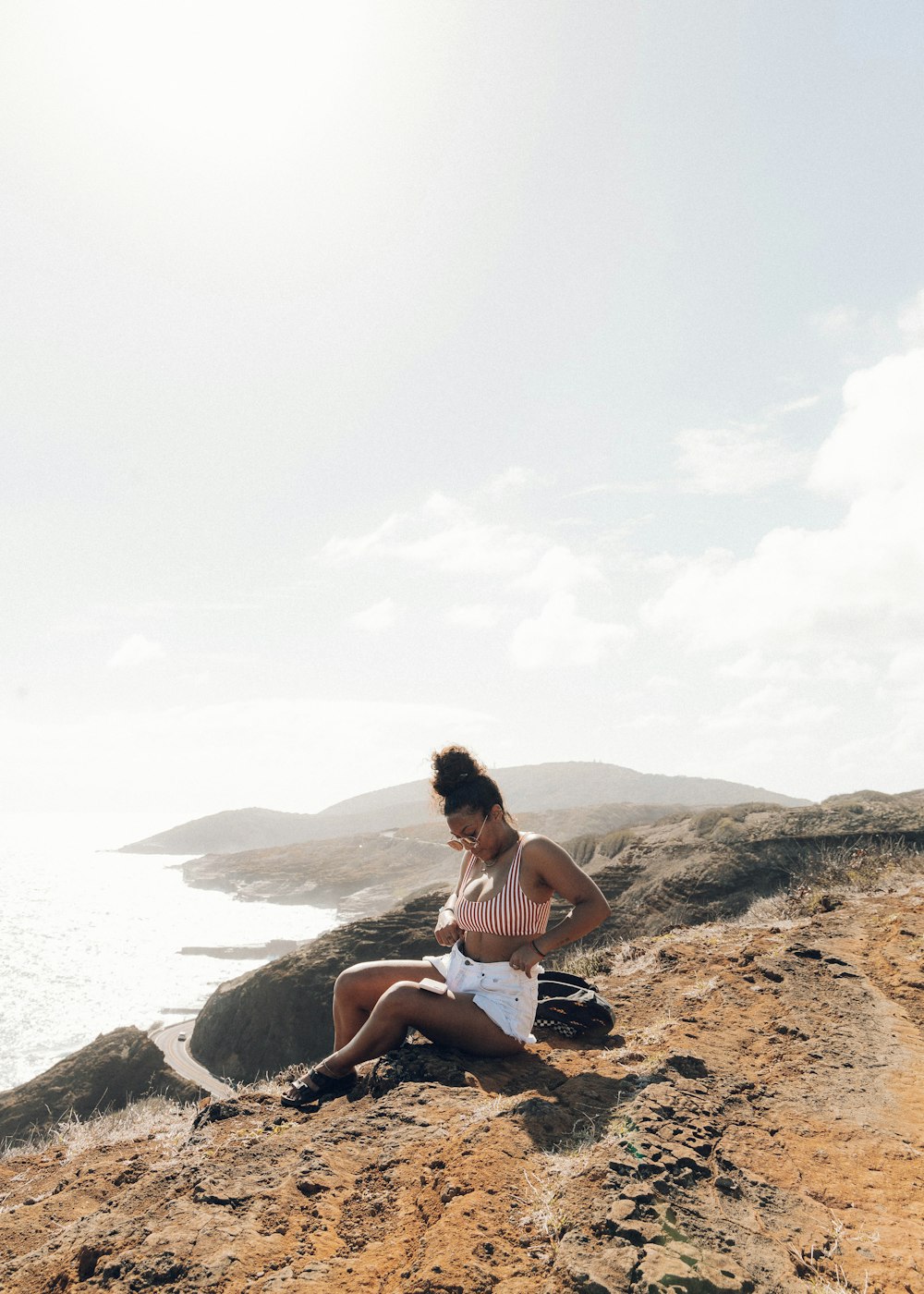 Mujer en camiseta blanca sin mangas sentada en una roca cerca del cuerpo de agua durante el día