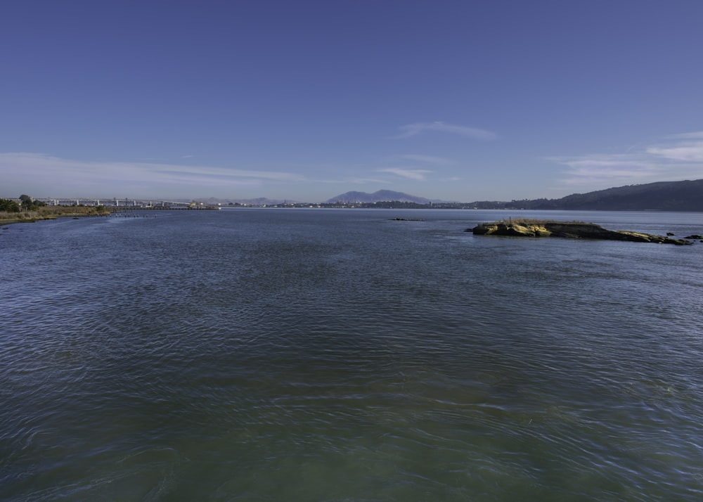 body of water near mountain under blue sky during daytime