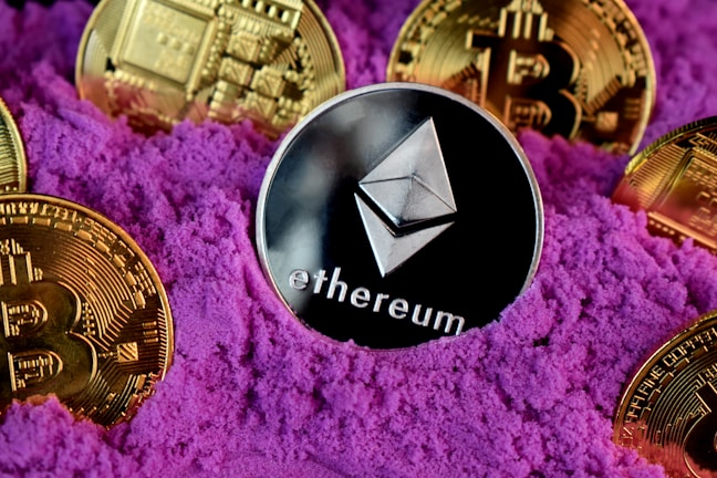 A collection of cryptocurrency coins, including Ethereum and Bitcoin, are partially buried in bright purple sand. The Ethereum coin is prominently featured at the center, while Bitcoin coins surround it.