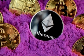 A collection of cryptocurrency coins, including Ethereum and Bitcoin, are partially buried in bright purple sand. The Ethereum coin is prominently featured at the center, while Bitcoin coins surround it.