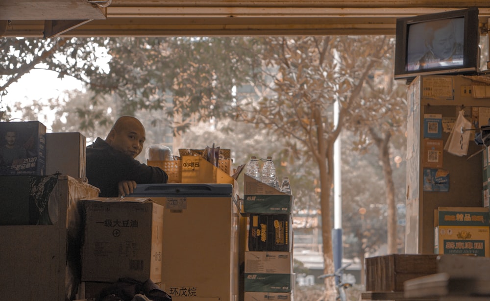 man in black jacket sitting beside brown cardboard boxes