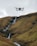 A drone hovers in the air against a backdrop of rolling hills with a small waterfall cascading down the rocky terrain.