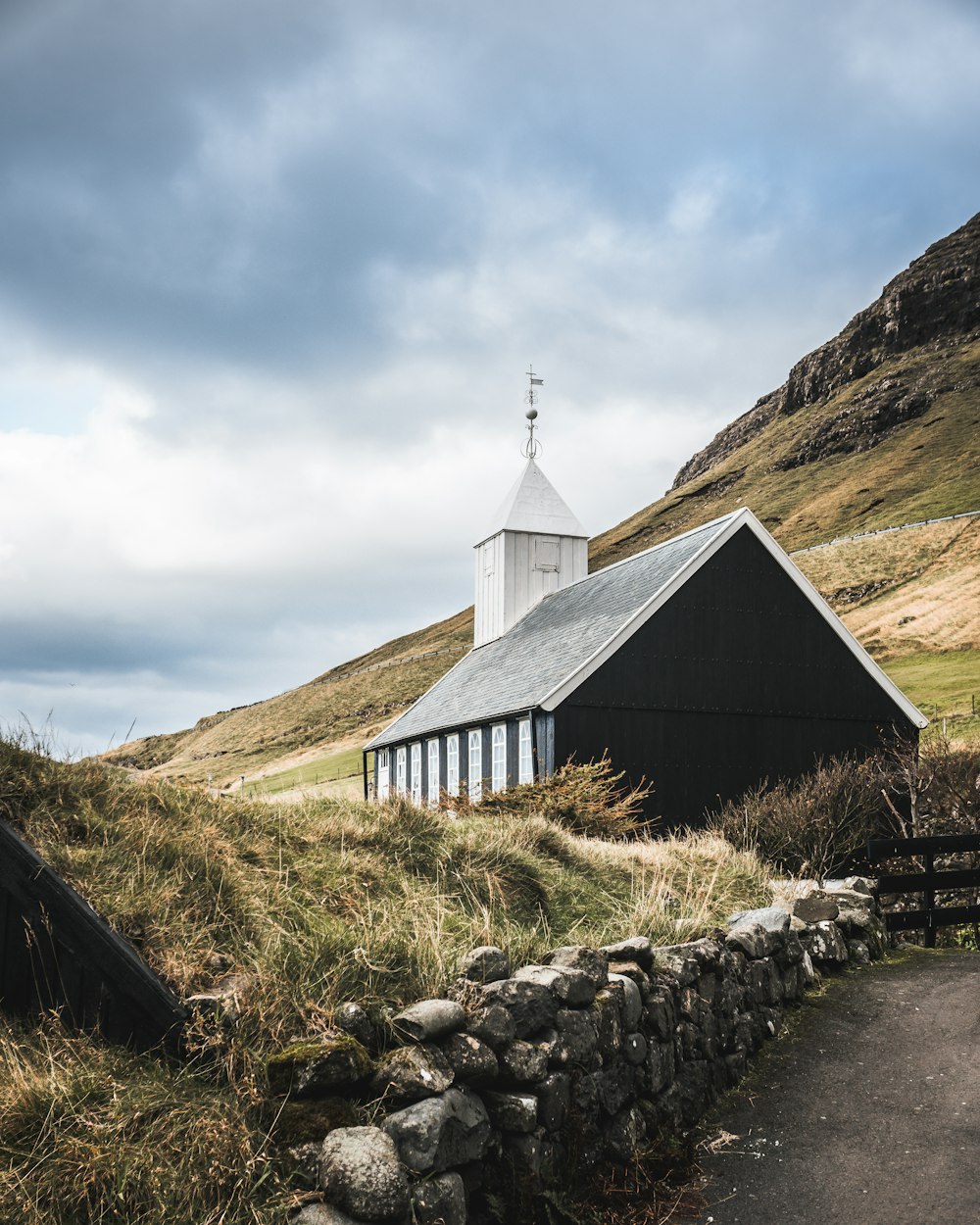 black and white concrete house on green grass field near mountain under white clouds during daytime