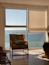 A cozy reading nook with sunlight streaming through a window overlooking the sea.