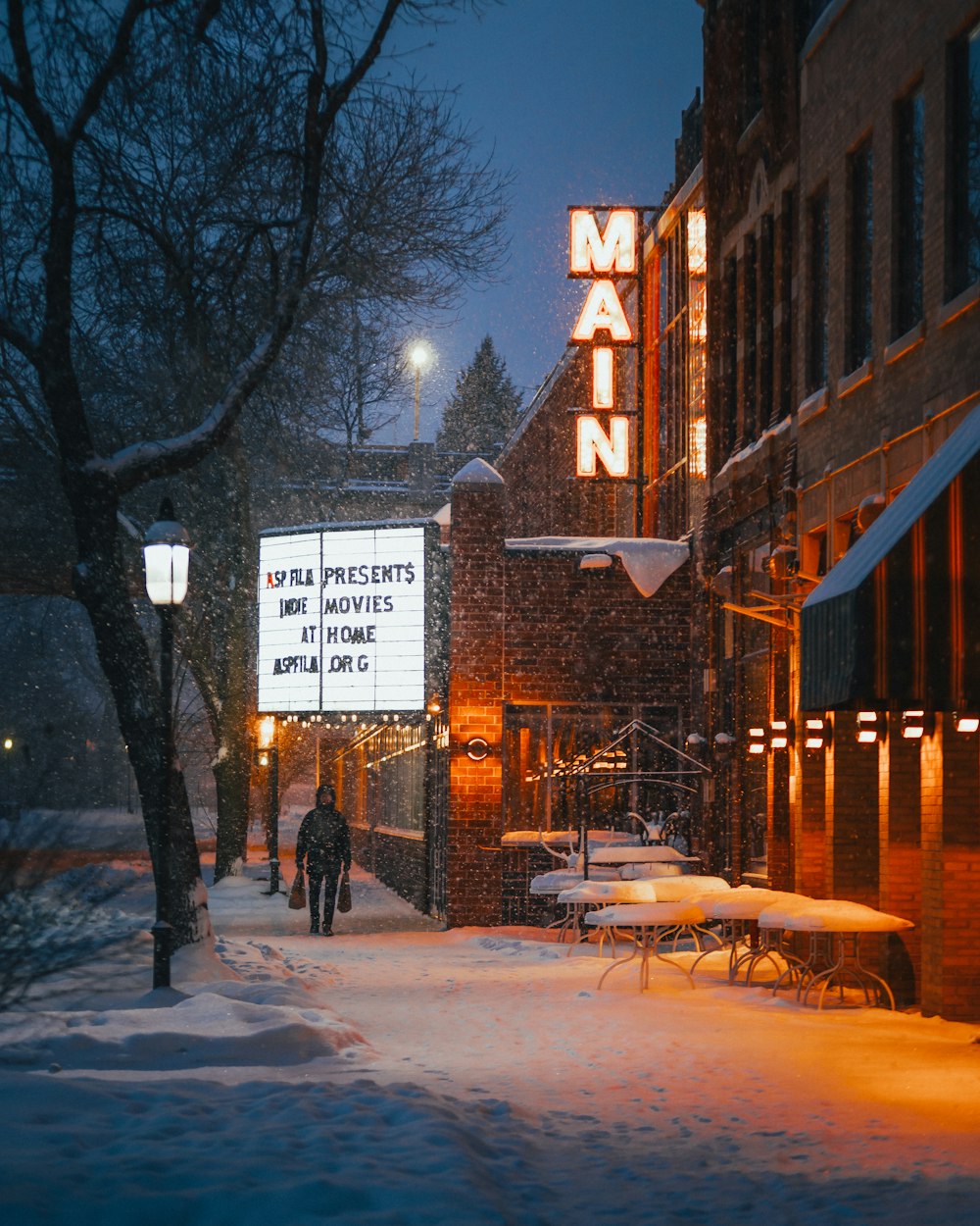 person walking on snow covered pathway near brown wooden bench during night time