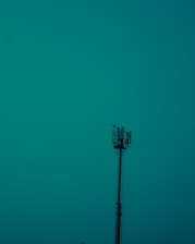 A tall communication tower stands prominently against a teal sky, with visible antennas and equipment at the top.