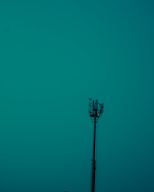 A tall communication tower stands prominently against a teal sky, with visible antennas and equipment at the top.