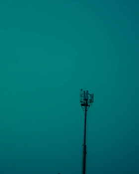 A tall communication tower stands prominently against a teal sky, with visible antennas and equipment at the top.
