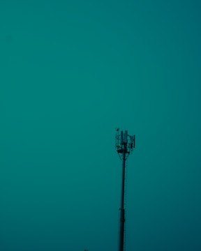 A tall communication tower stands prominently against a teal sky, with visible antennas and equipment at the top.